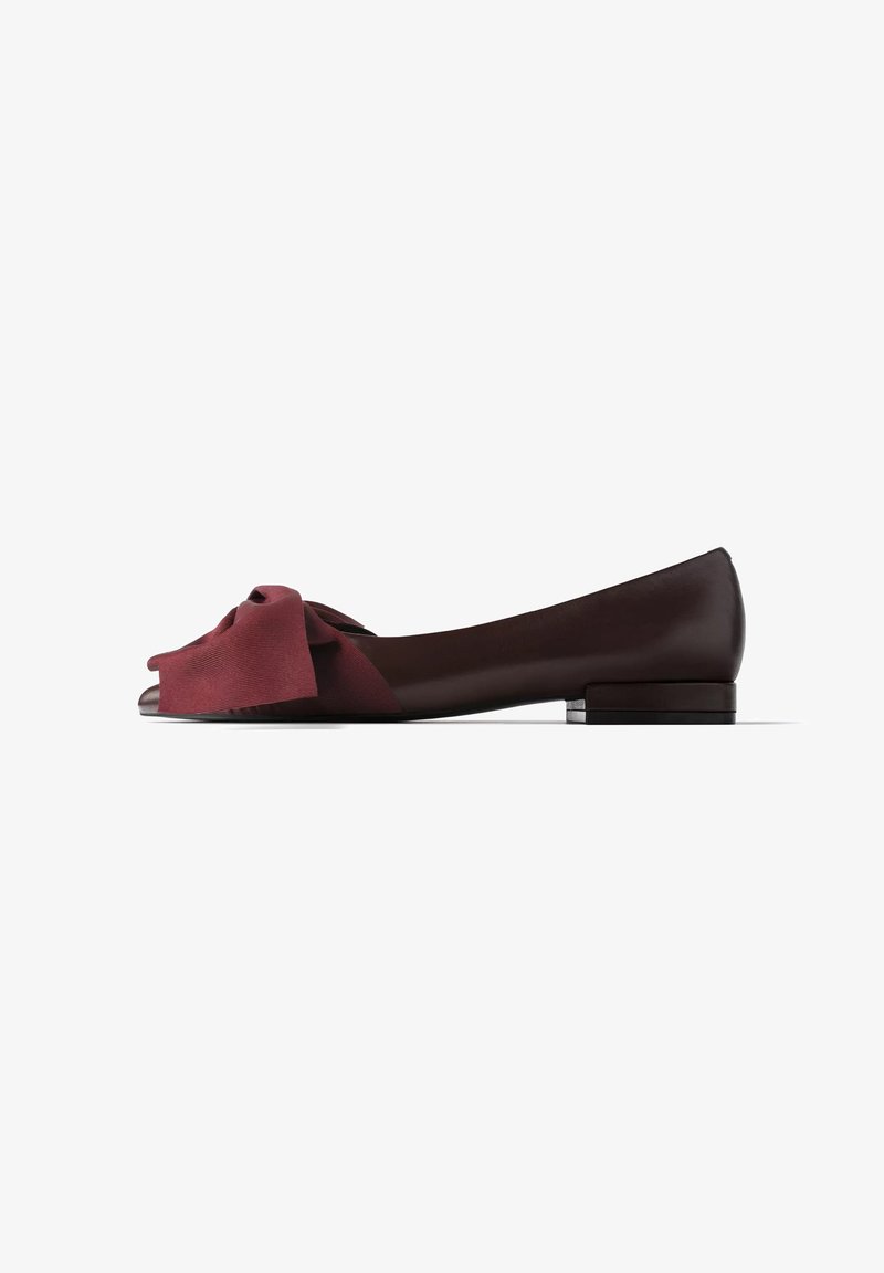Chaussure plate marron foncé avec un petit talon et un grand nœud en tissu bordeaux à l’avant, vue de côté sur fond blanc.