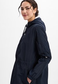 Marineblauwe lichtgewicht jas met een capuchon, trekkoord in de taille, ritszakken en elastische manchetten; gladde textuur en eenvoudig ontwerp.