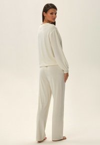 Biały zestaw odzieży do wypoczynku z prążkowanej tkaniny, zawierający długie rękawy i spodnie o prostym kroju. Miękka tekstura z luźnym fasonem, odpowiednia do codziennego noszenia.