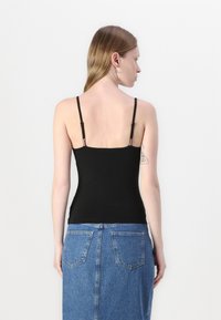 Black fitted tank top with thin adjustable straps, paired with a high-waisted denim skirt. Simple, seamless design, smooth texture.