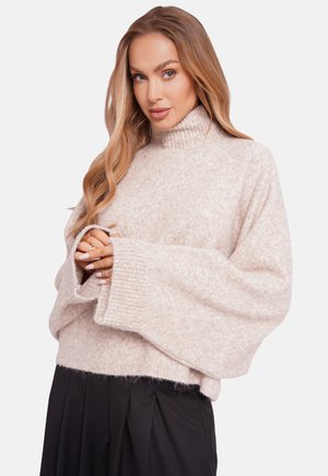 Jasnoróżowy, oversize sweter z wysokim kołnierzem, prążkowanymi mankietami i miękką, puszystą fakturą, połączony z czarnymi, plisowanymi spodniami.