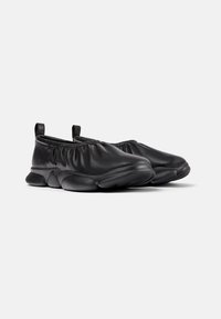 Sorte slip-ons laget av glatt lær med en samlet elastisk åpning og polstret gummisåle. Rund, bulbøs bunndesign.