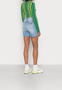 Farkkushortsit, joissa vaaleansininen pesu ja rispaantuneet reunat, yhdistetty vihreään ja keltaiseen raitaan pitkähihainen paita. Valkeat lenkkarit neonkorostuksilla.