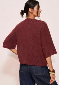 Burgundský pletený sveter s krátkymi rukávmi, okrúhlym výstrihom a voľným strihom. Textúrovaná tkanina s jemným vzhľadom a rebrovanými okrajmi.