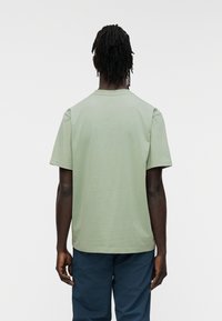 Πράσινο βαμβακερό t-shirt με στρογγυλή λαιμόκοψη και κοντά μανίκια, με άνετη εφαρμογή. Η πίσω όψη παρουσιάζει μια λεία, αδιάκοπη επιφάνεια.