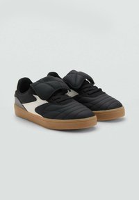 Sneaker nere imbottite con una texture liscia, dotate di un pannello laterale bianco e una suola in gomma naturale. Una fascia regolabile copre i lacci.