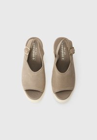 Brune lærred slip-on sko med åpen tå, justerbar gullspenne og kremfarget såle. Jevn tekstur med subtile detaljer.