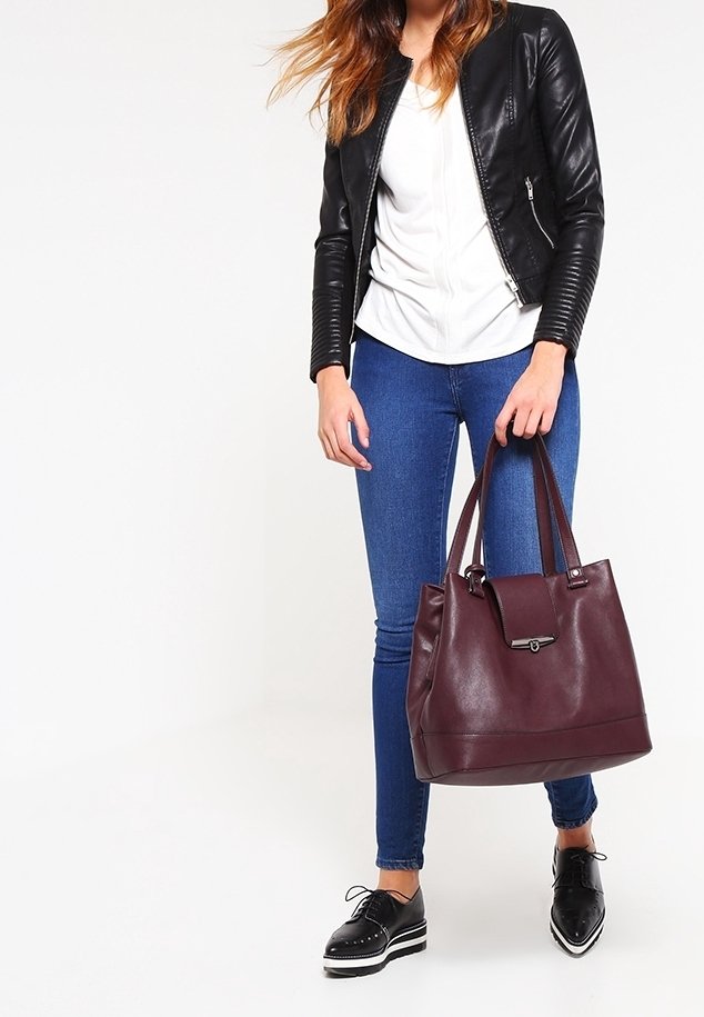 Burgundy leather tote bag with double handles, structured shape, and a metal clasp detail. Paired with dark jeans and a black leather jacket.