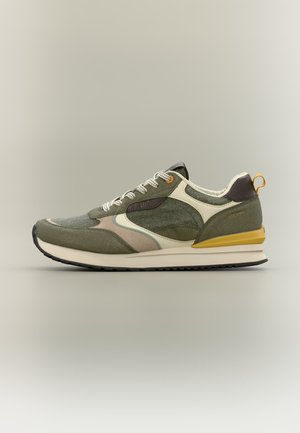Sneaker verde e beige con lacci bianchi, dettaglio giallo sul tallone e pannelli stratificati e testurizzati su uno sfondo neutro.