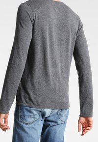 Szara koszula z długim rękawem wykonana z miękkiej tkaniny, z okrągłym dekoltem i dopasowanym krojem, zestawiona z niebieskimi dżinsami.