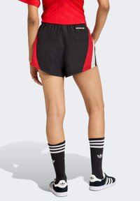 Crne i crvene sportske kratke hlače od teksturiranog tkanja, s bočnim akcentima u crvenoj i sivoj boji. Uparene s crnim čarapama s prugama i cipelama.