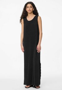 Juodas be rankovių maksi suknelė su tekstūruotu audiniu, apvaliu iškirpimu ir šonine plyšiu; derinama su juodais sandalais.