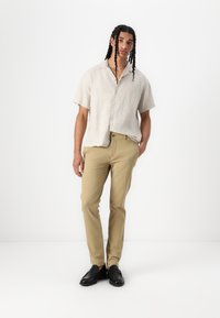 Lichtbeige shirt met korte mouwen, knopen aan de voorkant, gecombineerd met tan slim-fit broek en zwarte instappers. Glad textuur, casual pasvorm.