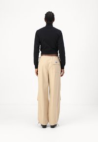 Black cropped jacket with high collar, paired with loose beige cargo pants featuring side pockets and drawstring waist.
