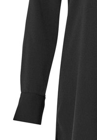 Czarna bluzka z długim rękawem o gładkiej, miękkiej fakturze; posiada mankiety zapinane na guziki i prosty krój, który podkreśla minimalistyczny design.