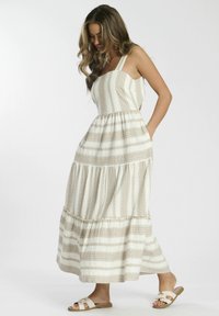 Vestido maxi con tirantes finos, de color crema con rayas verticales marrones y detalles similares a encaje; falda de capas con bolsillos; combinado con sandalias.