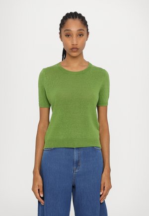 Pull en tricot vert à manches courtes avec un col rond, doté d'une texture lisse et d'un ourlet côtelé, associé à un jean bleu taille haute.