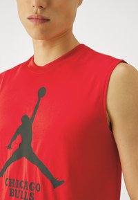 Rød ærmeløs T-shirt med en sort silhuet af en springende basketballspiller og teksten "CHICAGO BULLS" nedenfor.