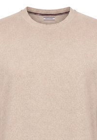 Pull beige col rond avec détail de col en côtes et étiquette de la marque Felix Hardy à l'intérieur de l'encolure.