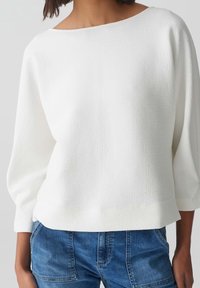 Pull blanc texturé avec un large col bateau et des manches trois-quarts, assorti à un short en denim bleu. Design simple et épuré.