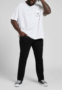 Biała bawełniana koszulka z kieszonką, z małym logo. Połączona z czarnymi dżinsami i czarno-białymi trampkami.