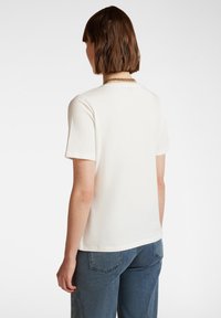 Camicia bianca a maniche corte realizzata in morbido cotone. Presenta un collo arrotondato. Abbinata a jeans in denim blu, che mostrano una vestibilità rilassata.