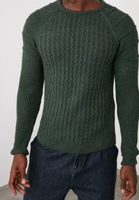 Donkergroene trui met getextureerd geribd patroon, ronde hals en lange mouwen. Met verhoogde stiknaden en aangesloten manchetten.