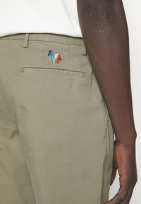 Spodnie khaki z tylną kieszenią ozdobioną wielobarwnym haftowanym wzorem konia. Materiał wydaje się gładki i lekki.