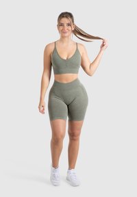 Olijfgroen sportoutfit bestaande uit een aansluitende, rekbare sportbeha en bijpassende shorts tot halverwege de bovenbenen, beide met een zachte textuur en minimale naden.