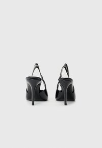 Black patent leather high-heeled shoes with a slingback design, featuring narrow straps and a distinct logo accent on the heel.