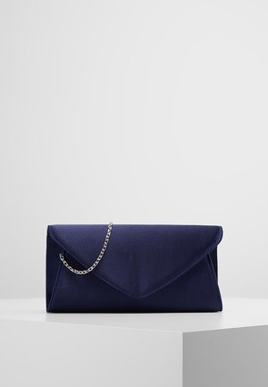 Navyblå satin clutch med trekantet klap og sølvkæderem, vist på hvid piedestal mod lys grå baggrund.