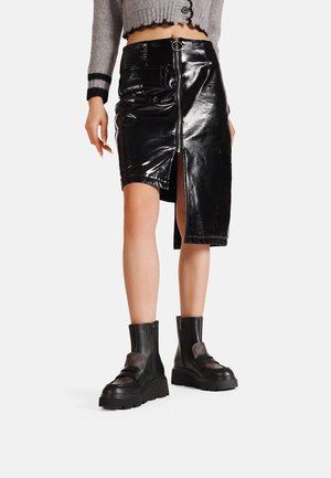 Gonna midi in finta pelle nera con chiusura zip frontale e uno spacco. Abbinata a stivali neri con tacco spesso e un maglione corto grigio.