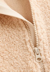 Fleece jacket in soft beige, featuring a chunky texture and a light fabric zipper. Inside showcases a smooth, cream lining.