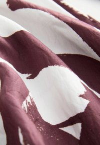 Stoff mit einem kastanienbraunen und weißen abstrakten Muster, mit weicher Textur und glatter Oberfläche, die Falten und Knicke zeigt.