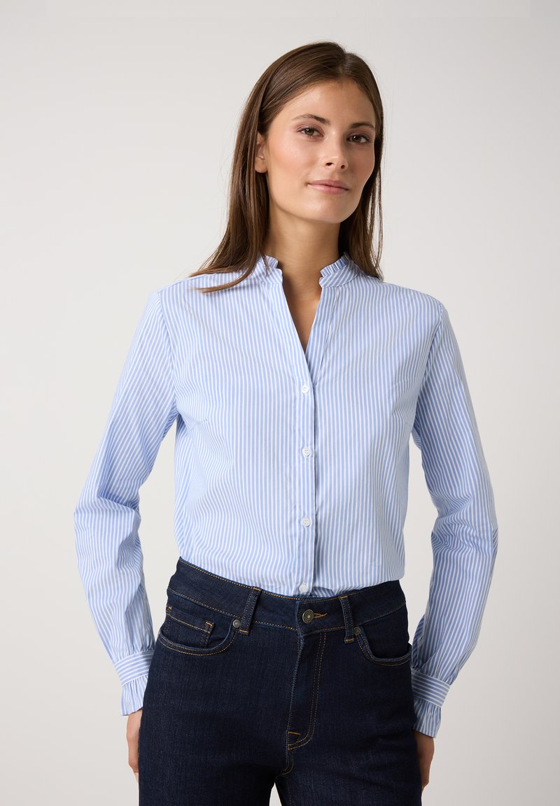Hellblau und weiß gestreiftes Button-Down-Hemd mit Stehkragen und langen Ärmeln, kombiniert mit dunkelblauen Jeans. Weiche Stofftextur.