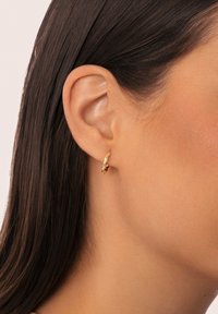 Goldene Creolen mit einem strukturierten, wellenförmigen Design. Kleine Größe, die das Ohrläppchen umschließt, mit einer glatten Oberfläche und einem polierten Finish.