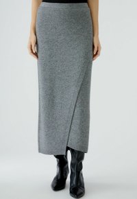Jupe maxi en tricot gris avec un design enveloppant, pr�ésentant une texture lisse et une taille côtelée, associée à des bottes noires ajustées.