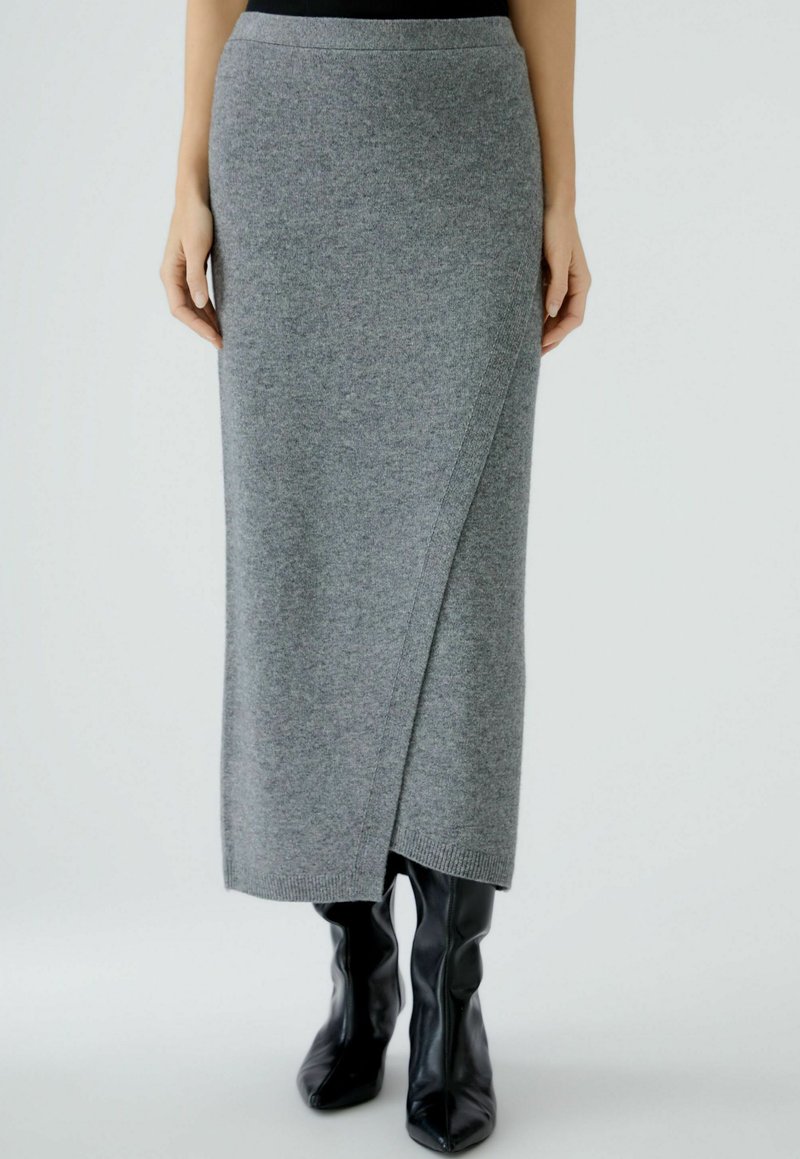 Jupe maxi en tricot gris avec un design enveloppant, présentant une texture lisse et une taille côtelée, associée à des bottes noires ajustées.