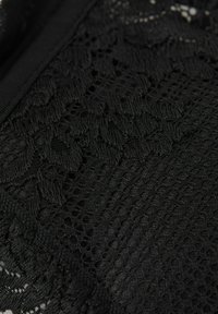 Svart tyg med intrikata spetsmönster och texturerade vävar, som visar kontrasterande släta och ribbade områden.