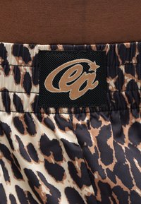 Ύφασμα με σχέδιο λεοπάρδαλης και μαύρη ορθογώνια ετικέτα με λογότυπο σε καφέ χρώμα και αστέρι ραμμένα στη συγκεντρωμένη μέση.