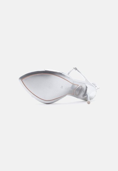 Ασημένιο σανδάλι στιλέτο με μυτερή μύτη, λουράκι στον αστράγαλο και τακούνι στιλέτο, εμφανιζόμενο από την πλευρά της σόλας σε λευκό φόντο.