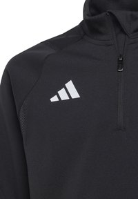 Zwarte sportieve zip-up jas met hoge kraag, voorzien van mesh accenten en een wit Adidas-logo op de linkerborst. Glad stoftextuur.