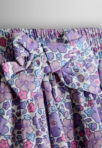 Detailný záber na látku s kvetinovým vzorom v odtieňoch fialovej, ružovej a modrej, s nariaseným pásom a detailom zaväzovacej mašle.