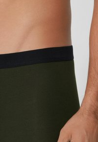 Dunkelgrüne Baumwoll-Boxershorts mit einem schwarzen elastischen Bund, die eine glatte Textur und ein enganliegendes Design aufweisen.