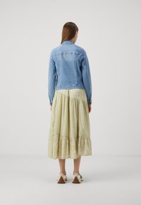 Chaqueta de mezclilla clara con un corte clásico, combinada con una falda de volantes con estampado en suaves tonos verdes. Los zapatos presentan un diseño contrastante.
