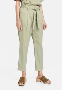 Jasnozielone, wysokie spodnie z zakładkami i wiązanym paskiem, o luźnym kroju i skróconych nogawkach, w połączeniu z brązowymi zamszowymi klapkami.