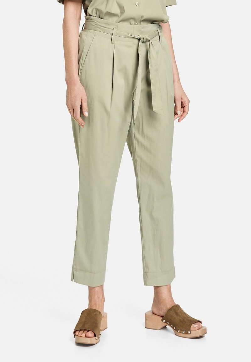 Jasnozielone, wysokie spodnie z zakładkami i wiązanym paskiem, o luźnym kroju i skróconych nogawkach, w połączeniu z brązowymi zamszowymi klapkami.