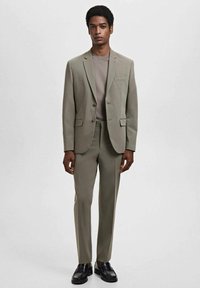 Light gray suit made of textured fabric, featuring a single-breasted jacket with two buttons, straight-leg trousers, and black shoes.