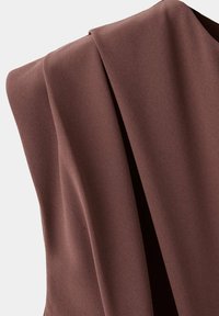 Tissu marron avec des plis doux et une texture lisse, drapé sur un fond neutre.