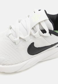 Chaussure de sport blanche avec une texture à côtes verticales, logo Swoosh noir et accents noirs au niveau du col et des lacets. Conception légère.